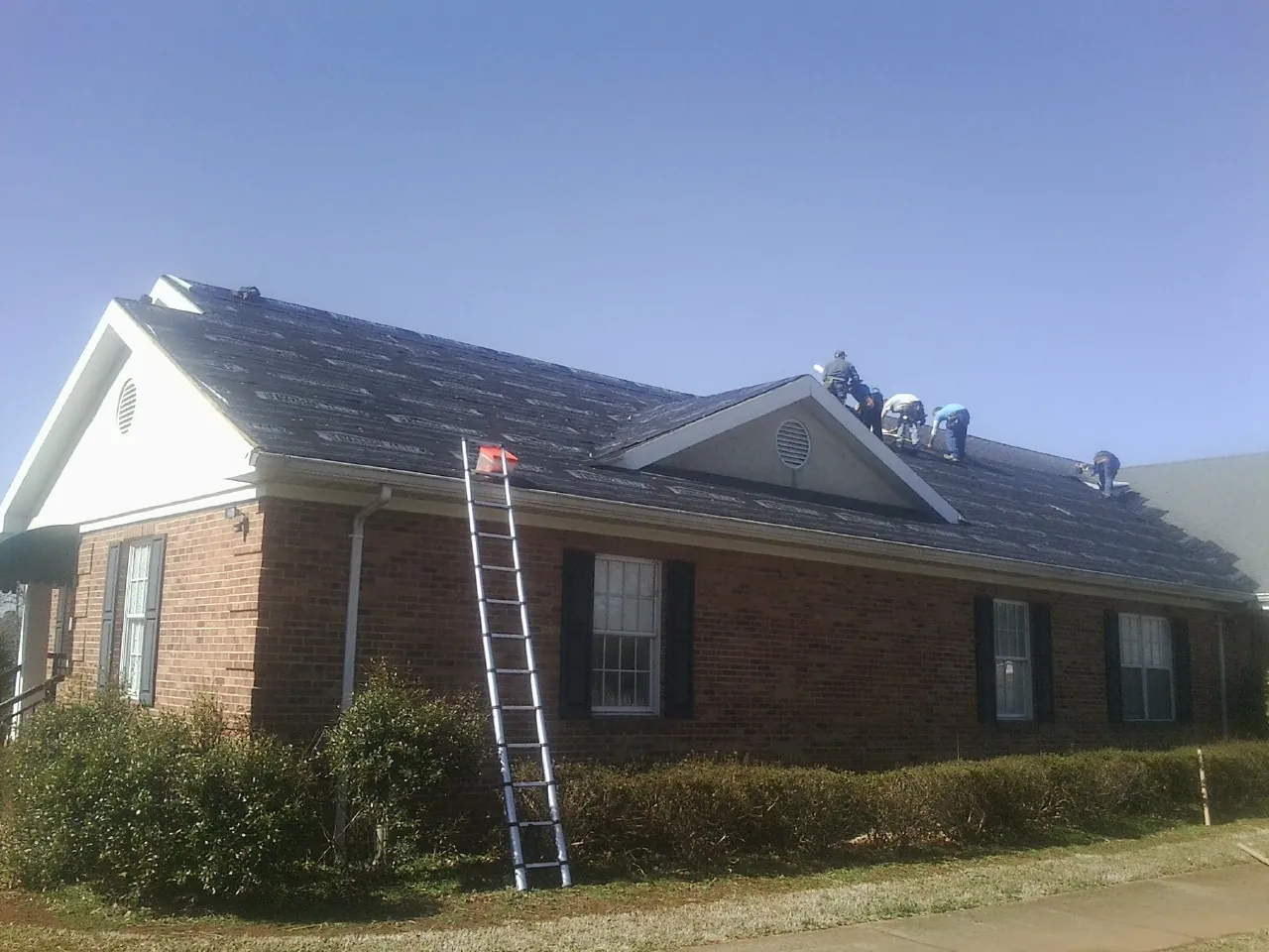 Crew tearing shingles off a brick ranch roof with a ladder set — Metal Roof Repair work by our crew in Long Beach