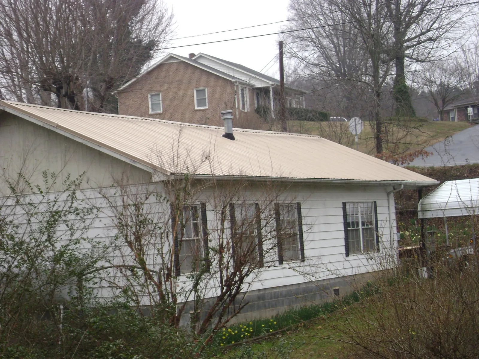 Tan metal roof on a white sided house set into a hillside — Commercial Roofing by Roofing Brothers in Long Beach